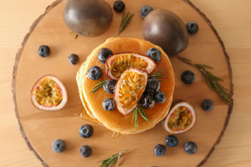 Tasty pancakes with passion fruit and berries on wooden board