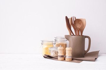 Set of kitchen utensils with groats on table near white wall