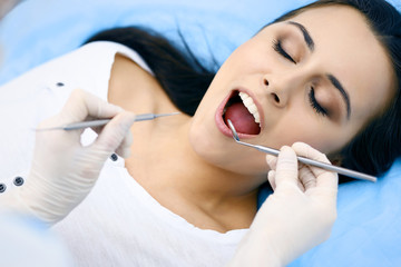 Young female patient visiting dentist office.Beautiful woman with healthy straight white teeth sitting at dental chair with open mouth during oral checkup while doctor working at teeth