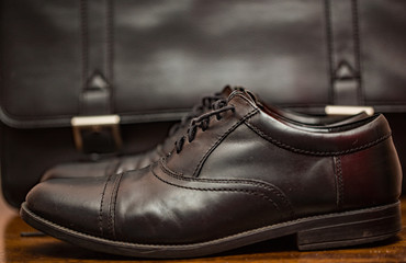 Cose up of a pair of black leather lace up business shoes in front of a matching black leather case