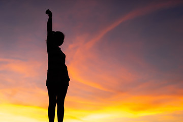 Fototapeta premium The silhouette of the woman is standing, holding hands relaxed with success at sunset.
