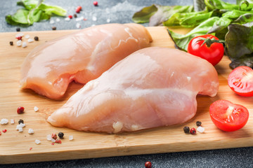 Raw chicken breast fillet with greens, tomatoes and spices on a dark background.
