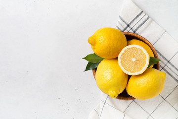 Ripe lemons in bowl with leaves on white background