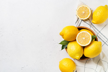Ripe lemons in bowl with leaves on white background