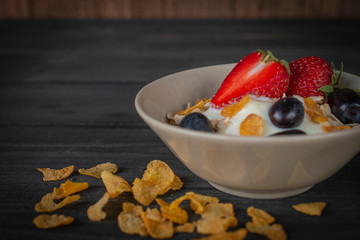 Yoghurt mix oatmeal, strawberry and grape topping in white bowl on the wood table with cornflakes placed in front of.