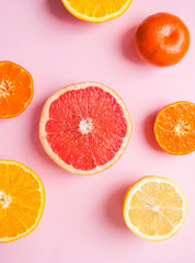 Flat lay of cut ripe juicy grapefruit, lemon and orange on pink background. Citrus pattern.