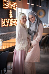 Two young muslim smiling women standing in the cafe