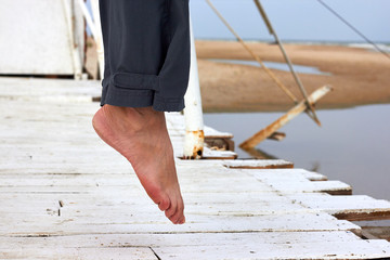 Legs of a woman hovering in the air over a white wooden pier. Woman's tiptoes. - obrazy, fototapety, plakaty