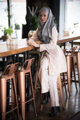 A young muslim woman sitting on a bar chair in a cafe