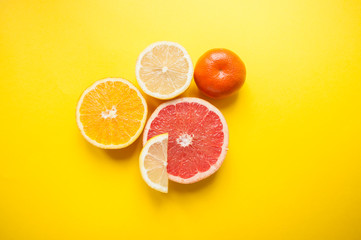 Flat lay of cut ripe juicy grapefruit, lemon and orange on yellow background. Citrus pattern.