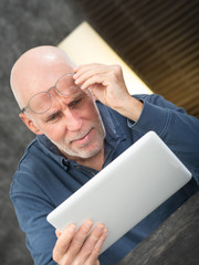 Senior man using tablet, he is having difficulties and vision problems
