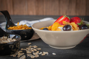 Yoghurt mix oatmeal, strawberry and grape topping in white bowl on the wood table with Blue and white striped fabric, oatmeal, cornflakes and milk in glass placed around.