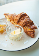 Delicious and nutritious french breakfast. Fresh croissant with jam and butter on grey table in a cafe.