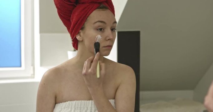 The movie of happy young woman applying clay mask on her face, in bathroom. Beauty treatment.