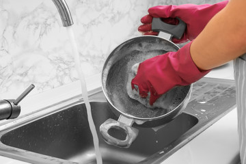 Woman washing saucepan in kitchen sink