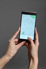 Woman holding mobile phone displaying map on screen against grey background