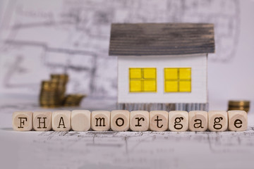Abbreviation FHA mortgage composed of wooden letters. Small paper house in the background.