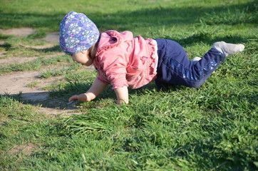 Smiling cute playful little girl is standing on green grass. girl toddler walks around the lake learns to walk. sunny sping or summer day
