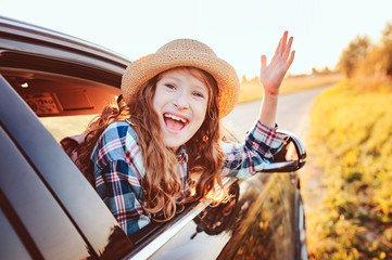 happy child girl looking out the car window during road trip on summer vacations. Summertime, exploring new places concept