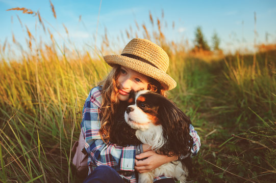 happy child girl enjoying summer vacations with her dog, walking and playing on sunny meadow. Traveling, exploring new places and rural living concept