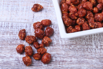 Sugared Hazelnuts in a white bowl on a wooden background. Hazelnuts in sugar glaze. Selective focus.