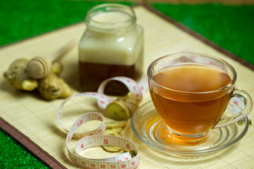 Ginger juice in a clear cup and honey jar placed beside with measuring tape..Concept of healthy.