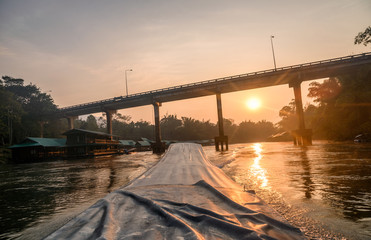 Sailing long-tail boat with sunrise on bridge in river kwai