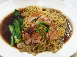 Top view of egg noodle with shrimp wontons and roasted duck topped with sliced scallion on white plat