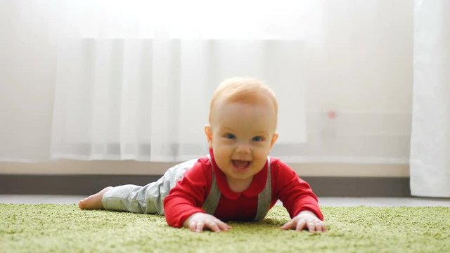 Baby Crawls Toward Rack Focus Low Angle Slow Motion. Baby crawls toward the camera in slow motion smiling and laughing in a white room