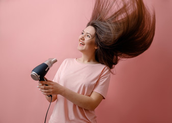 young smiling woman with hairdryer in hands on pink background strong wind hair flight