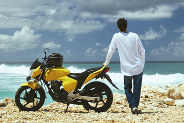 Fototapeta na wymiar Young handsome man standing near motorcycle on the tropical beach.