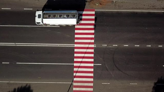Truck is passing through the crossing with red and white stripes painted on black asphalt. Top view of crosswalk for pedestrians in the road at daytime. Aerial view