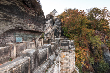 Fototapeta na wymiar Bastei bridge in the national park Saxon Switzerland. Elbe sandstone mountains. lateral panoramic view on historical brickwork of fortress with rock formations and trees in autumn.