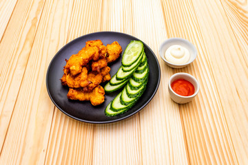 Chicken fried (nuggets) homemade on black plate with two sauces - mayonnaise and hot spicy sauce. On wooden background