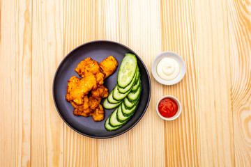 Chicken fried (nuggets) homemade on black plate with two sauces - mayonnaise and hot spicy sauce. On wooden background, top view