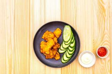 Chicken fried (nuggets) homemade on black plate with two sauces - mayonnaise and hot spicy sauce. On wooden background, top view