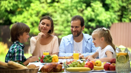 Parents and children sitting at table, enjoying family dinner, having fun, joy