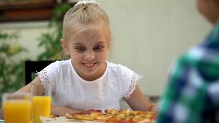 Smiling girl looking at pizza and choosing best slice, family food traditions