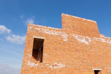 wall of an unfinished house on a background of blue sky, a wall of red brick