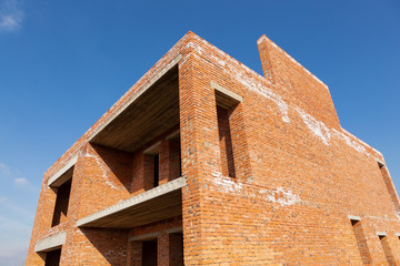 fragment of an unfinished brick house against the blue sky, concept of construction