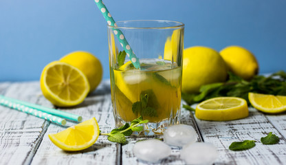 Summer refreshing drink in a glass. Traditional cold sweet-sour lemonade with lemon, mint and ice cubes on a gray wooden table.