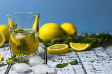 Summer refreshing drink in a glass. Traditional cold sweet-sour lemonade with lemon, mint and ice cubes on a gray wooden table.