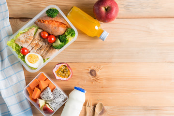 Healthy lunch boxes in plastic package, Grilled chicken breast with sweet potato, egg and vegetable salad, fruit, orange juice, milk. Diet food concept. Top view and Copy space.