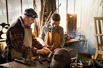 A craftsman in his workshop teaches his work to his apprentice - obrazy, fototapety, plakaty