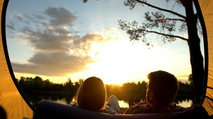 Loving pair resting and watching sunset, enjoying moment, view from inside tent