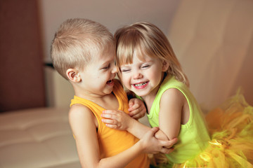 cute smiling children, brother and sister, 2-3 years old, pogodki, a girl in a tutu skirt, dressed in bright yellow colors playing on the couch and hugging