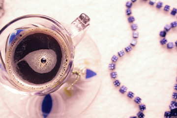 coffee in a transparent cup and beads on a white fur background in violet colors