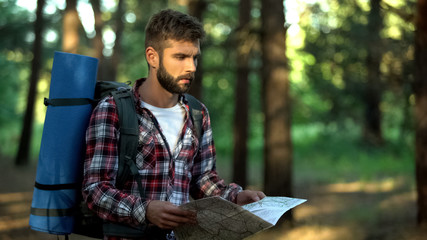 Confused hiker lost in forest tries to read map for directions, emotional stress