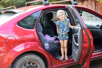 small child (blonde girl) 4 years out of the red car with a car seat came from far away and be happy