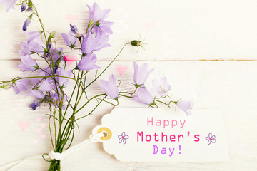 Mothers day card with with a bouquet of delicate wildflowers campanula on white wooden board